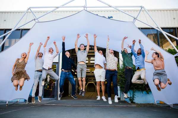 Group of people jumping in front of a Konligo Fastival event structure with a white membrane cover, celebrating outside a modern industrial building, now available on MTN Shop US.