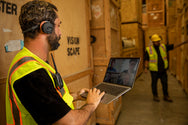 Warehouse worker wearing Sena EXPAND Mesh headset using laptop on loading dock - imagen 7